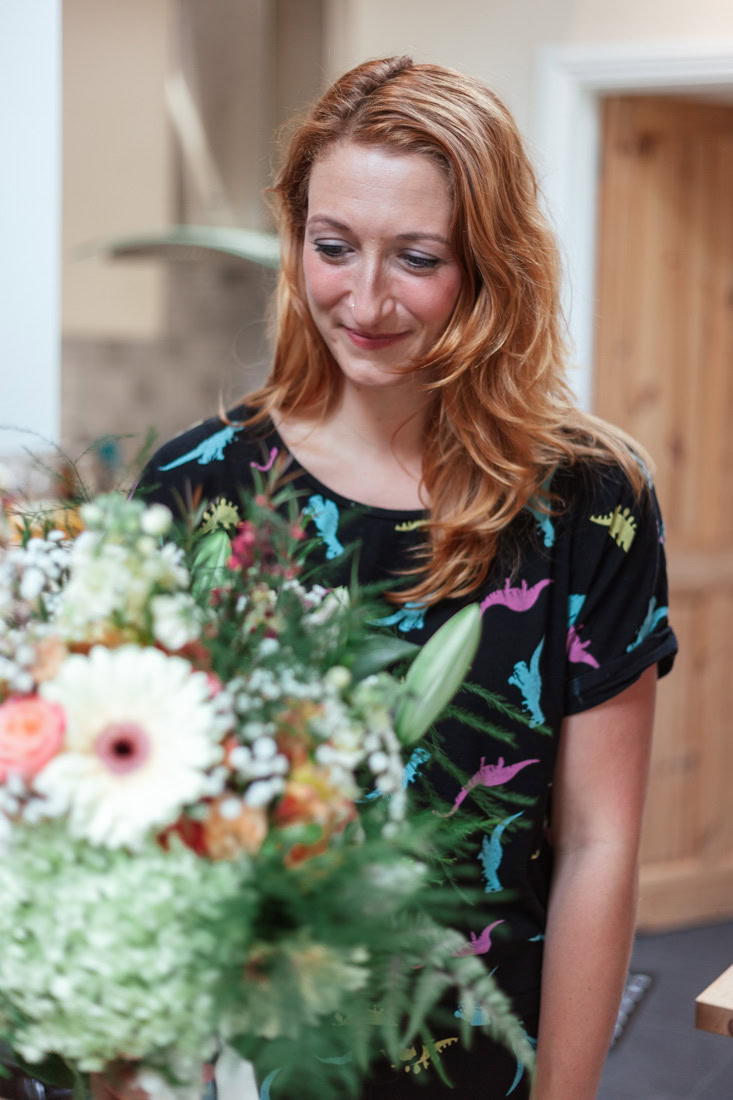 Person with long hair in a dinosaur-print shirt holds a colorful bouquet with mixed flowers and greenery.