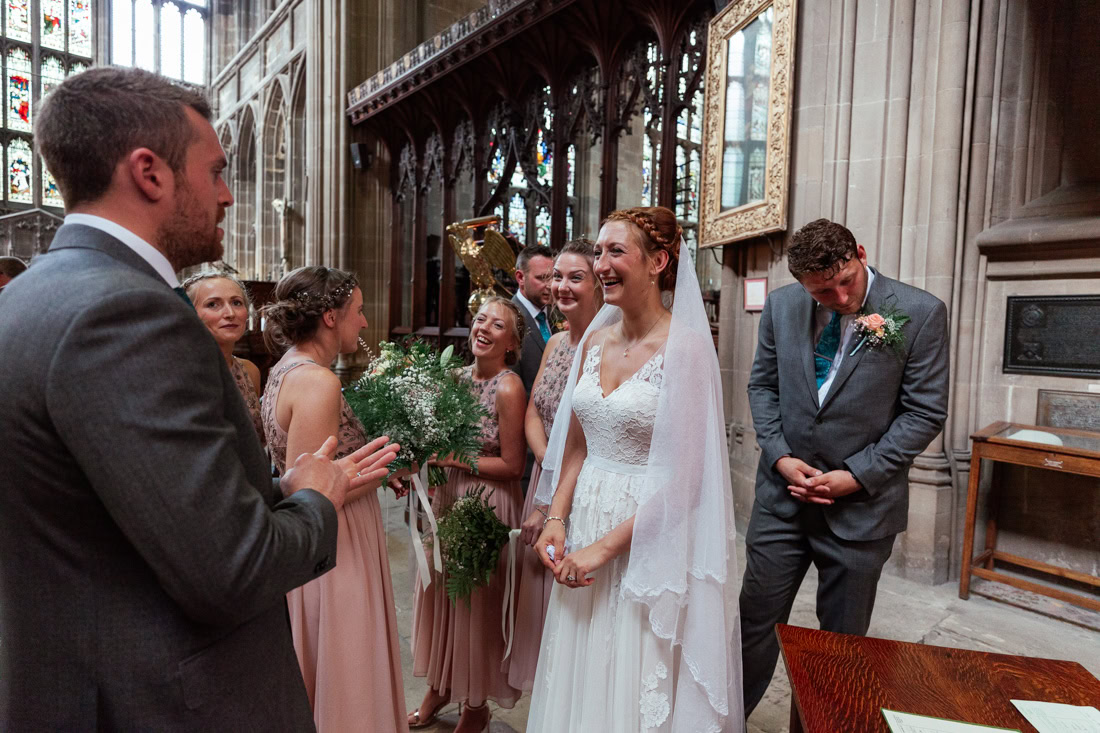 Bride in white dress stands with bridesmaids in pink and a groomsman inside a church during the wedding ceremony.