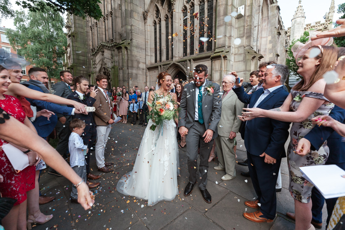 Wedding couple walks through cheering guests outside a church as confetti fills the air in celebration.