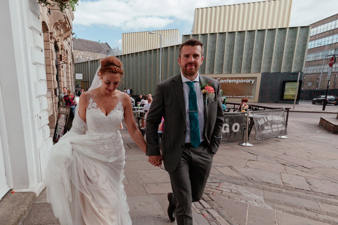 Bride and groom walk hand in hand past a modern art building the nottingham contempory.