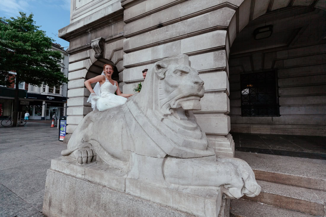A bride is sitting smiling on the left lion outside the nottingham council house repection venue.
