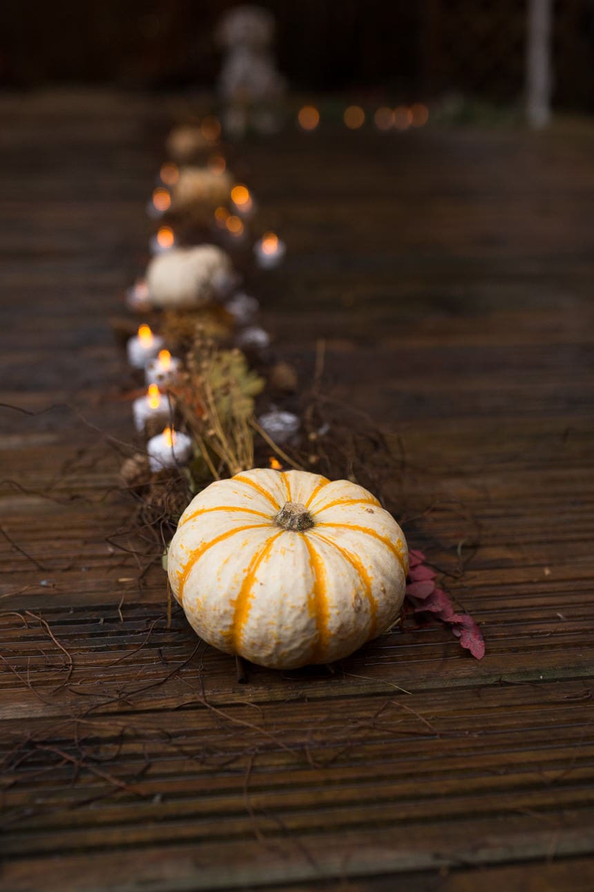 Striped white pumpkin on a wooden deck surrounded by candles and dried autumn foliage.