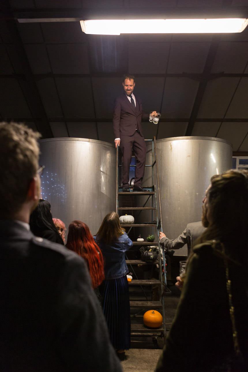 groom making a speech stood on top of a set of ladders holding an empty pint glass at the Beartown Brewery