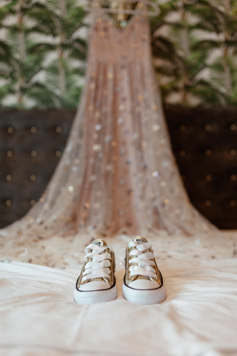 golden converse trainers laid on the bed infront of the pink wedding gown