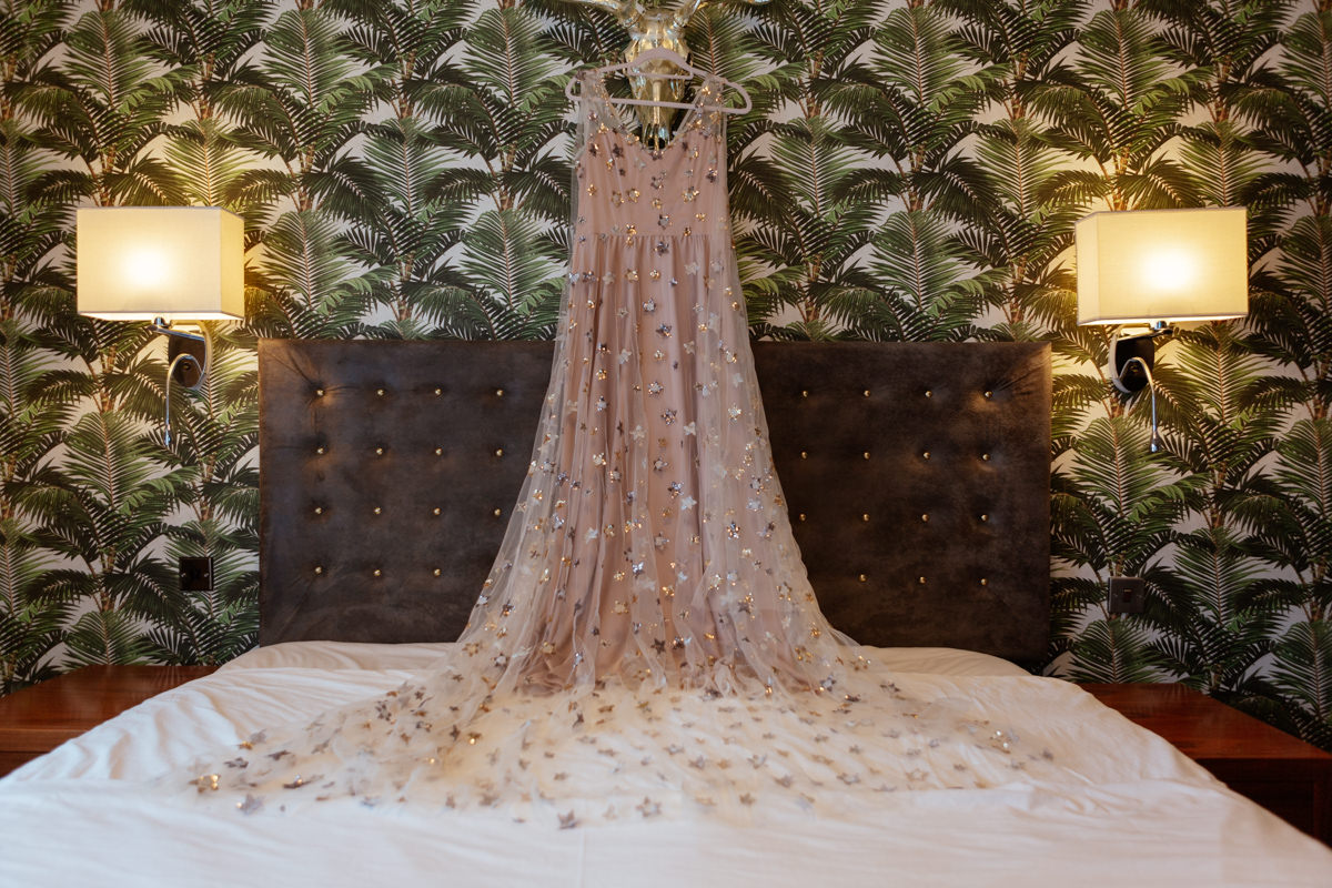 pink wedding gown hanging on the wall from a set of golden antlers, the dresses train is spread over the bed
