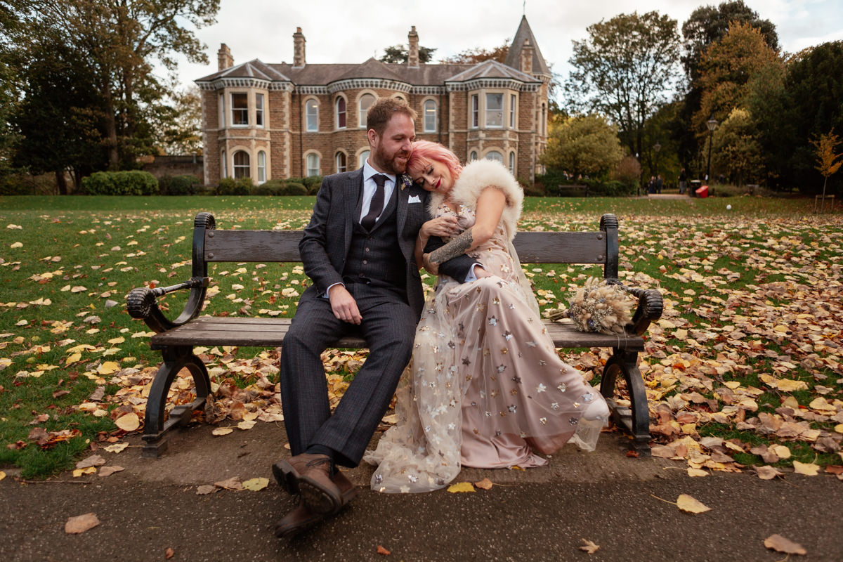 Pink‑haired person hugs someone tightly in Arno Vale Park, sharing an emotional moment on the grass.