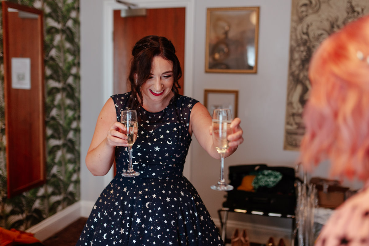 woman stood smiling holding two glasses of champagne, passing one to another woman