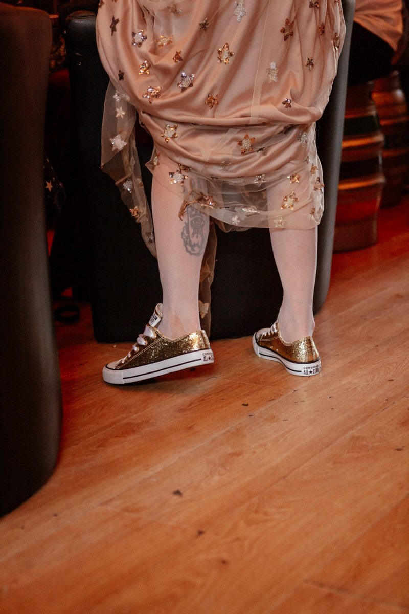 Person in a star-covered dress stands indoors wearing gold glitter Converse sneakers.