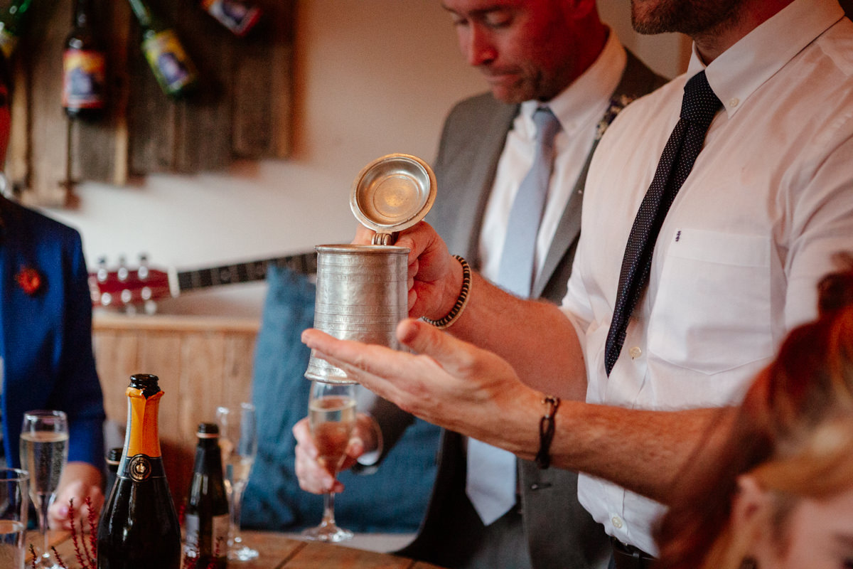 A group of people in formal wear gather around a table as someone shows a pewter tankard.