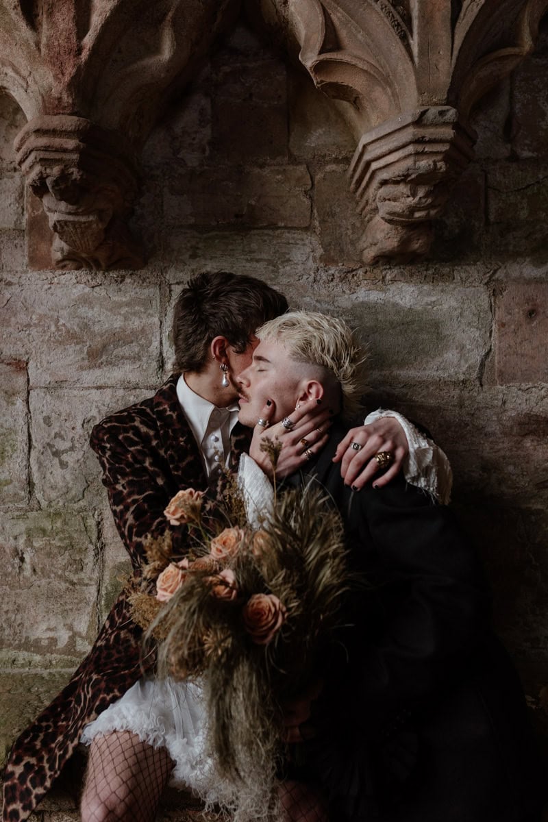 Two people embracing inside Dunglass Collegiate Church, holding dried flowers against carved stone walls.