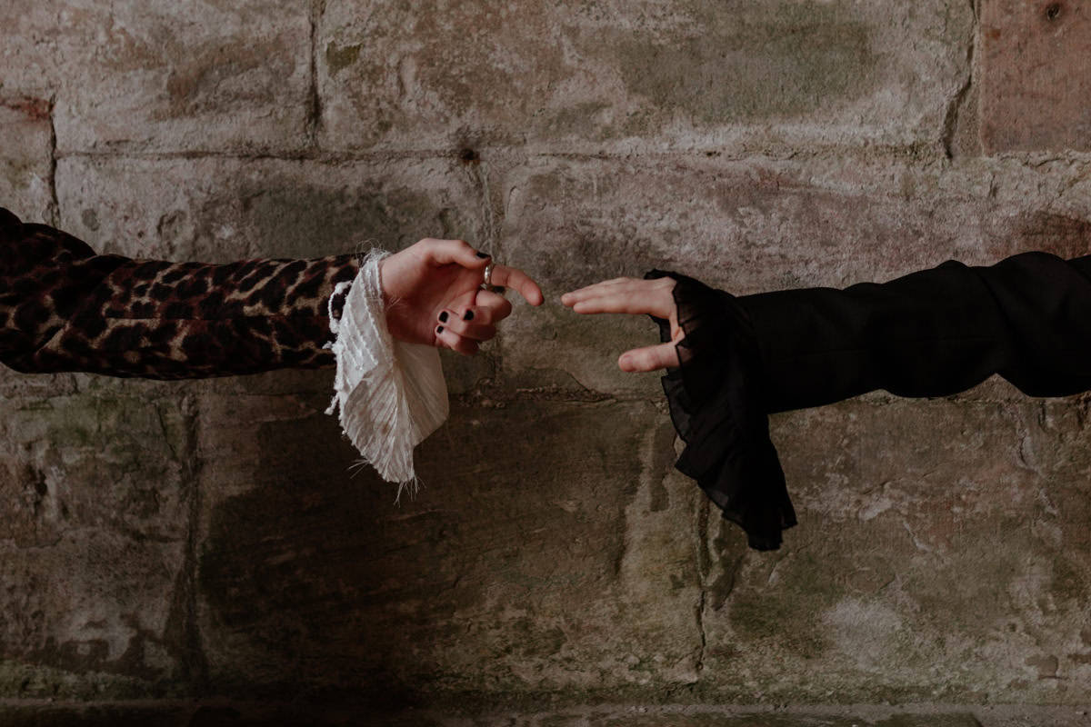 Two hands reaching toward each other against a textured stone wall, fingers nearly touching.