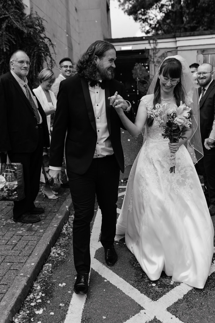 Bride and groom walk hand-in-hand, smiling amid guests at their Arnot Hill House wedding celebration.