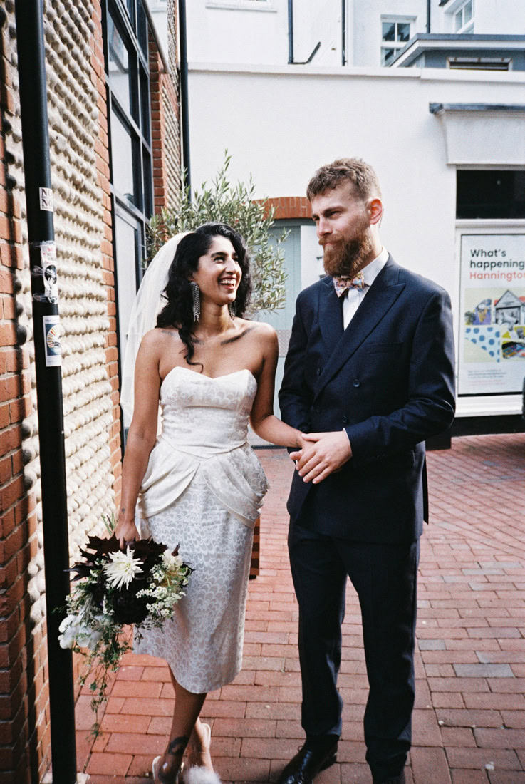 Bride and groom hold hands on a brick walkway laughing, the image has texture from 35mm film
