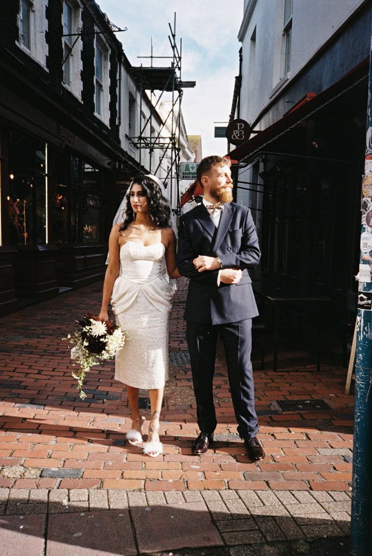 Couple pose on brick street in formal wear, looking in different directions in a stylish wedding moment