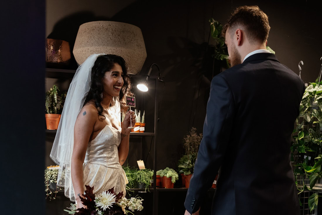 Bride holds a sun lover sign smiling at the groom inside a plant shop called Hugo and Green