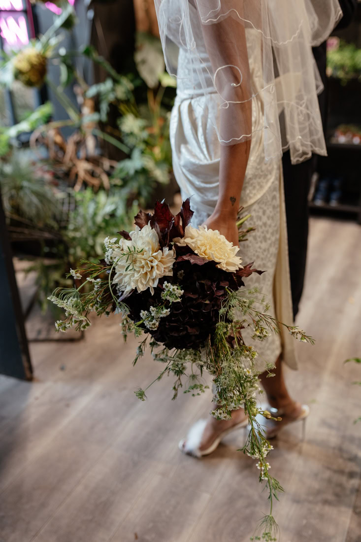 Close-up of bride holding a purple and cream bouquet; veil and fluffy high heels visible.