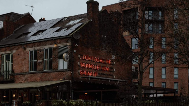 Brick pub with solar panels and neon sign: DON'T DO ALL THE TALKING, LET LOVE SPEAK UP