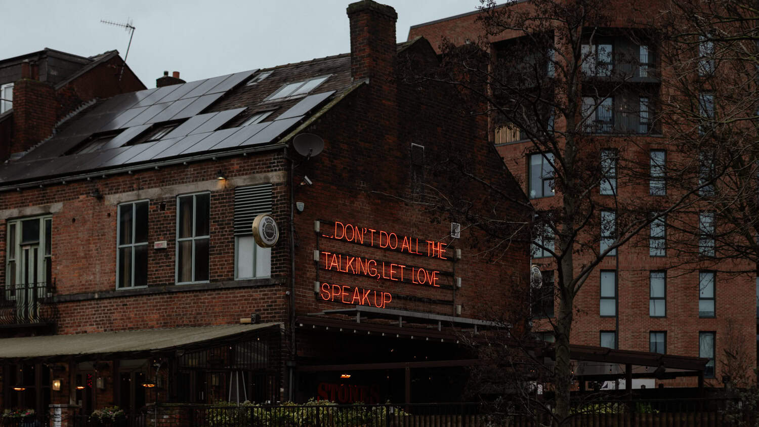 Brick pub with solar panels and neon sign: DON'T DO ALL THE TALKING, LET LOVE SPEAK UP
