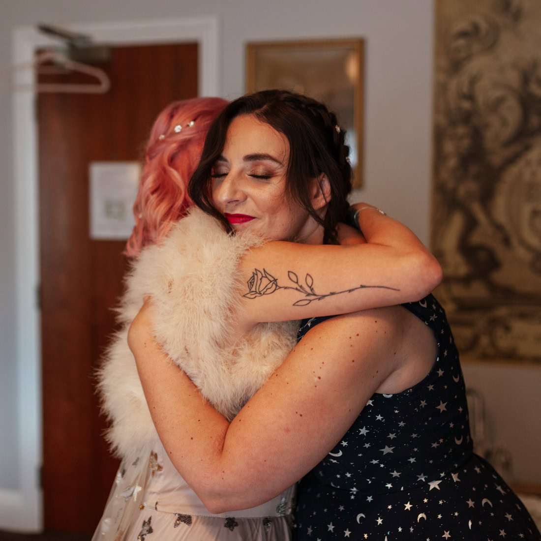 Two people share a warm hug in a room, one in a light dress and the other in a dark star‑patterned outfit.