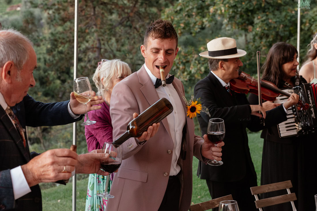 Joyful outdoor Italian wedding with people raising drinks, playing music, and enjoying the moment together.