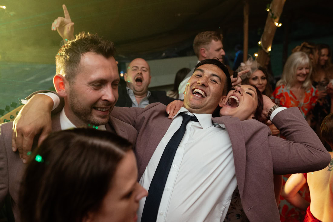 Smiling friends pose closely together at a lively wedding evening reception.