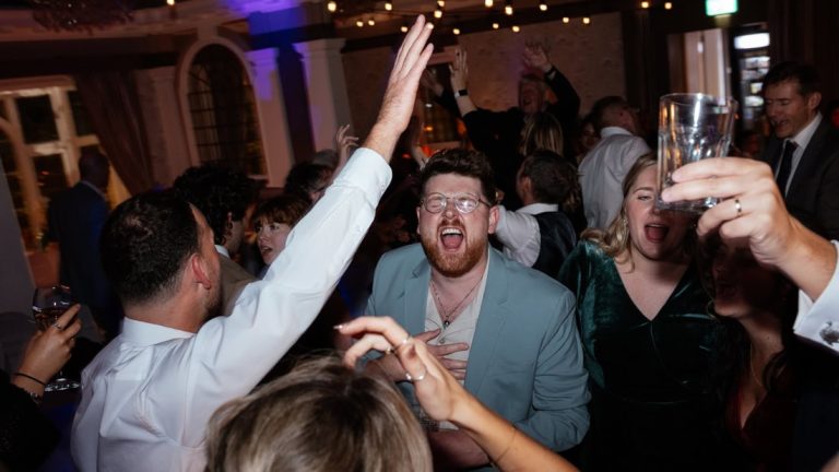 People dance and raise their hands in a lively, warmly lit embankment pub wedding celebration.