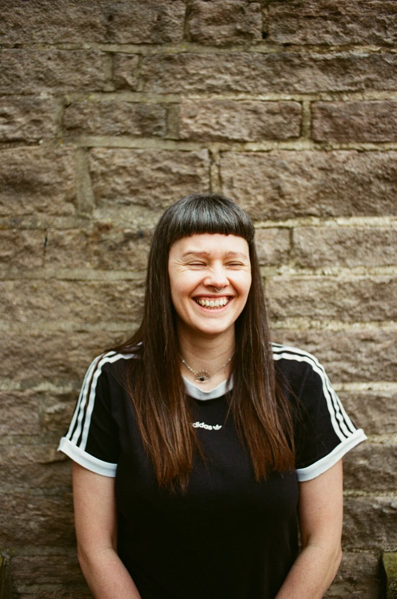 woman in adidas t-shirt laughing in front of a brick wall