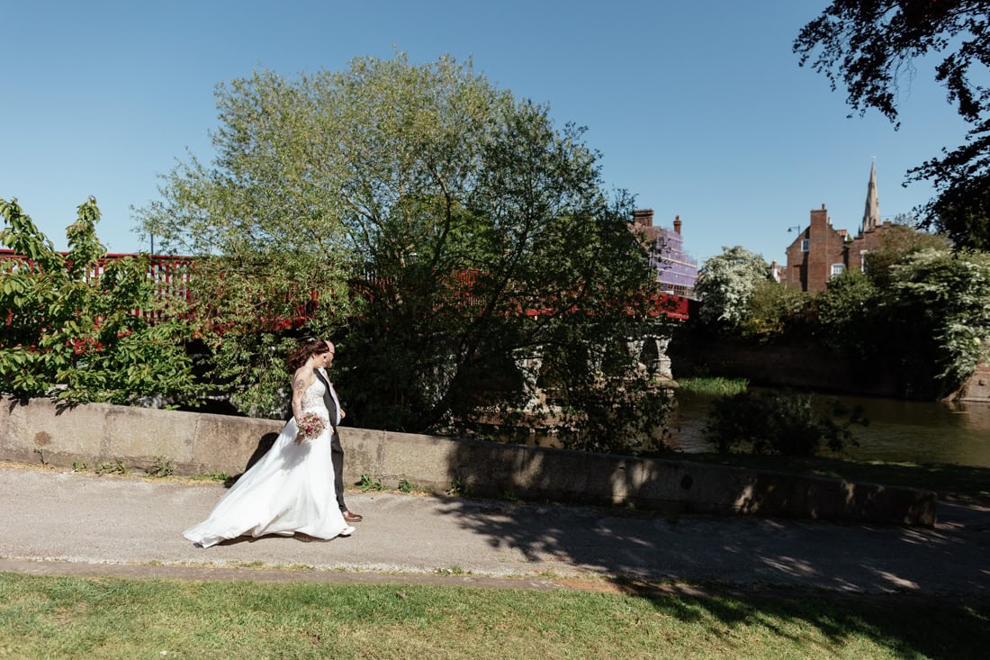 Couple walk along the Newark canal one in a wedding dress holding a bouquet and the other in a suit.